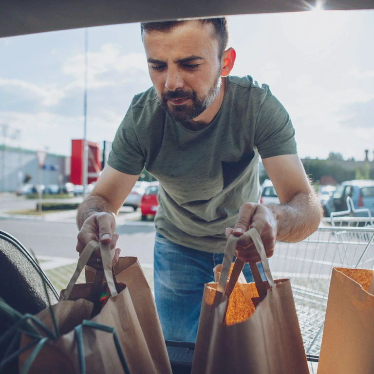 człowiek wkładający zakupy do&nbsp;bagażnika